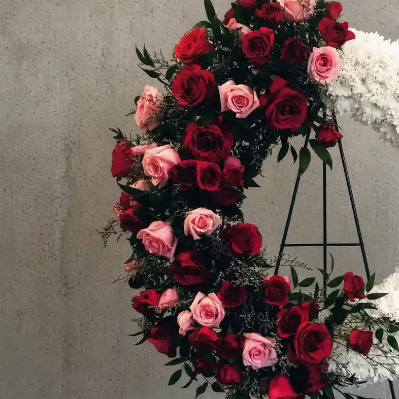 Close-up of the XL arrangement: oval wreath with a crescent of red and pink roses and white chrysanthemums