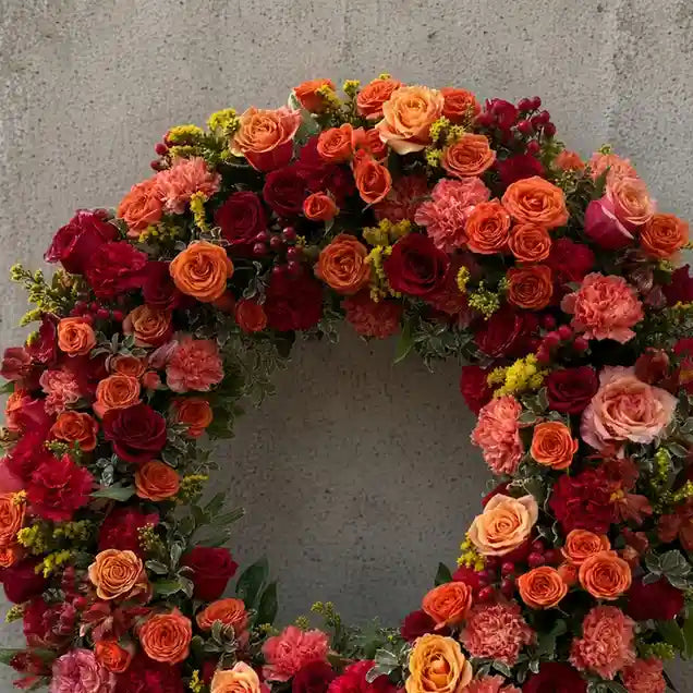 Close-up of the XL arrangement: orange and red wreath of roses, carnations and solidago